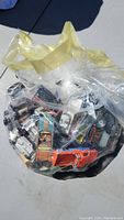 Plastic bag filled with multiple assorted toy cars in various colors including orange, yellow, and blue.
