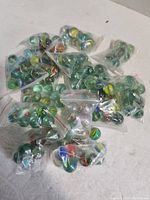 Photo showing multiple small clear plastic bags filled with assorted glass marbles, placed on a flat surface with white background.