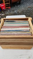 Wooden crate filled with various vinyl records, showing the spines and covers of the records inside.