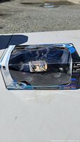 Side view of unopened collectible car in clear plastic window box, showing the black car with beige interior and slight package damage.