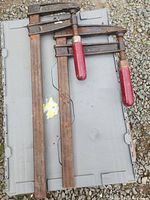 Overview photo showing two weathered bar clamps lying on a plastic container. Both have rust on their bars and red handles. The clamps are fully extended and show the long metal bars and cast iron clamp heads.