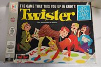 Front cover of Twister board game box showing cartoon illustrations of people playing the game on a colorful mat with red, yellow, green, and blue dots.