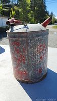 Front angle photo of the vintage metal jerry can showing rust and faded red markings with handle and spout.