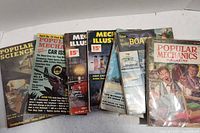 Photo showing a stack of eight vintage magazines including Popular Mechanics, Popular Science, Mechanix Illustrated and How to Build Boat magazines.