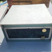 Top and front side view of vintage record player showing textured cream top and teal sides with black control panel and two knobs.