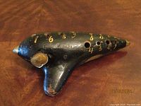 View of the full ocarina showing 11 holes, gold numbers, and overall shape including mouthpiece and body curvature.