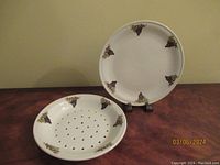 Two-piece porcelain set with a grape motif: round strainer dish with drainage holes and matching bottom plate.