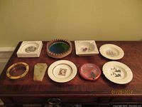 Nine collectible ash trays arranged on a wood surface, showing diverse shapes, colors, and styles.