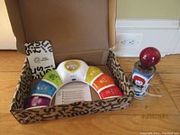 Photo showing Baby Einstein musical toy inside original box and vintage Raggedy Ann and Andy soda can lamp side by side on floor.