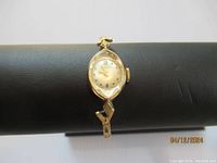 Front view of the vintage Benrus ladies watch on a black display stand showing the oval dial and gold case.