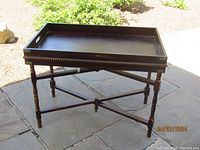 Front angle view of the vintage wooden campaign tray table showing the tray with carved trim and removable feature, supported by foldable turned legs in an X-shaped base.