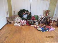 Wide view of all Christmas decor including Santas, wrapped gift boxes, wreath, various ornaments, gift bags and lights on wood floor against white doors.