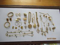Full group of costume jewelry items laid out including necklaces, earrings, rings, pendants and brooches in gold-tone metal with some faux gemstone accents.