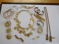 Overview of group of gold-tone costume jewelry including bracelets, brooches, and necklaces on a table.