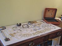 Overview photo of all costume jewelry items laid out on dresser surface including necklaces, bracelets, rings, pins and wood box