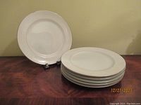 Photo showing full set of 6 white dinner plates with visible embossed decorative pattern on the rim.