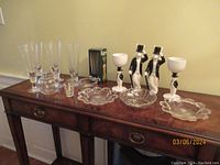 Photo of four clear pilsner glasses, one boxed Carlsberg pilsner glass, three scalloped edge glass dishes, two ceramic tuxedo rabbit figurines holding white goblets, two plastic tuxedo rabbit figurines on table