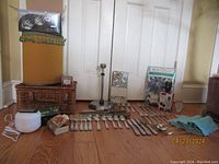 Photo showing various home goods including basket, diffuser, silver utensils and table linens on floor