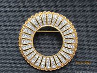 Front view of the circular gold-tone JBK brooch with clear rhinestones in a radiating pattern.