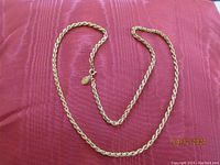 Top view of KJL gold-tone rope chain necklace arranged on red fabric background showing length and clasp with KJL charm.