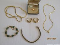 All items displayed on flat surface: two gold tone necklaces, gold tone hoop earrings, 6-link stone Krementz bracelet with safety chain, vintage tie tack in box