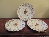 Set of three Limoges France dinner plates on wooden table, showing full plates and floral design