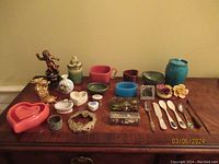 Group of various vintage and decorative items displayed on wooden surface including trinket boxes, figurines, flatware, and decorative jars and dishes.
