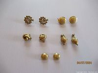 Five pairs of gold tone Monet earrings in a single photo arranged in rows on a white background showing diversity in design and signed style.
