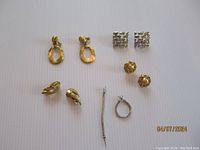 Five pairs of Monet earrings arranged on white background showing gold tone and silver tone styles including various shapes and closures.