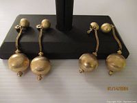 Front view of two sets of Monet gold tone ball drop earrings displayed on black stand showing textured balls and chain details