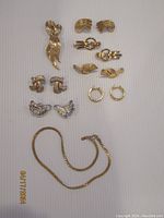 Full set including six pairs of gold tone Monet earrings arranged in three columns, one bow/knot-shaped gold tone brooch, and the necklace.