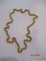 Photo of the entire gold plated rolo chain necklace laid out on a white textured surface showing the full length and thick rounded links.