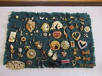 Full view of large group of assorted vintage pins on dark blue-green fabric background showing variety of shapes, styles, and colors.