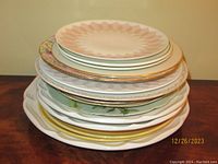Stack of mixed replacement plates showing various sizes and edge designs including gold trim and floral patterns