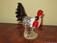 Front angle showing black and white patterned body, red comb and wattle, clear legs on wooden surface.