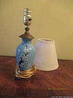 Blue ceramic lamp with floral pattern and white fabric lampshade set on wooden surface