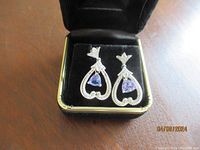 Photo of the pair of tanzanite and diamond drop earrings with a platinum finish, displayed upright in a black velvet jewelry box.
