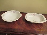 Photo of two TK Thum porcelain bowls, one round and one square, on wooden surface showing floral patterns and side handles.