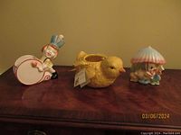 Three ceramic planters on a wooden surface including Stanford Drum Major, yellow duck, and clown with umbrella.