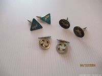 Overview photo showing all three sets of cuff links: triangular blue enamel set with gold fairy, round silver knot weave set, and round black enamel set with gold design.