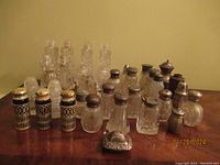 Group shot showing multiple vintage salt and pepper shakers with some featuring tarnished sterling silver caps and detailed glass bodies.