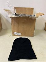Opened box with black toque hat on table beside it to show condition and material.