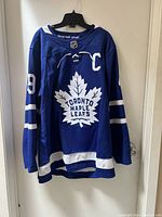 Front view of blue Toronto Maple Leafs Adidas NHL jersey with large maple leaf logo and captain 'C' badge.