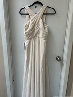 Full view of off white dress hanging on a hanger showing crossed straps back design and ruched bodice.