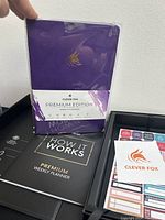 Front view of Clever Fox Premium Edition Weekly Planner with purple cover and gold fox logo, accompanied by instruction booklet and sticker sheets.