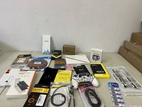Lot overview showing multiple electronic and cell phone accessories including screen protectors, cables, battery pack, adapters, and charger boxes