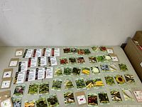 Wide assortment of seed packets laid out on a table showing many different vegetable and flower varieties
