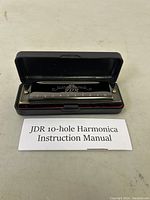 Harmonica inside open black plastic case with instruction manual in front.