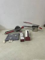 Two Bellemain potato mashers with red handles, electric milk frother and bottle opener in boxes, and hot plate towel arranged on table.