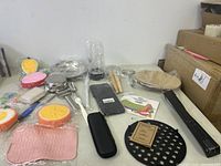 Image shows a collection of new kitchen items including trivets, utensils, a blender cup, and other accessories arranged on a surface.